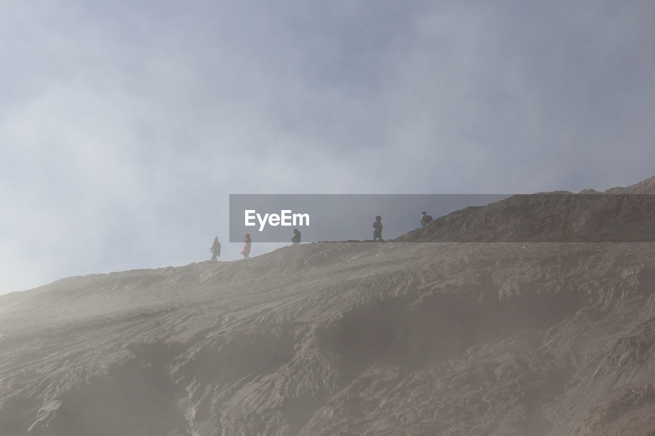 Low angle view of people standing on rocky mountain against sky