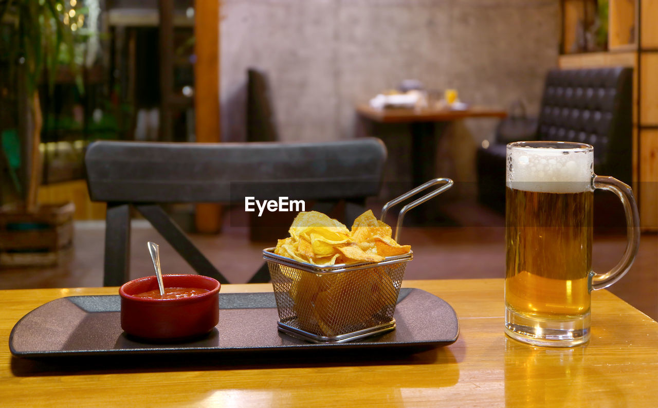 A basket of potato chips and dip with a glass of chilled draft beer on the wooden table