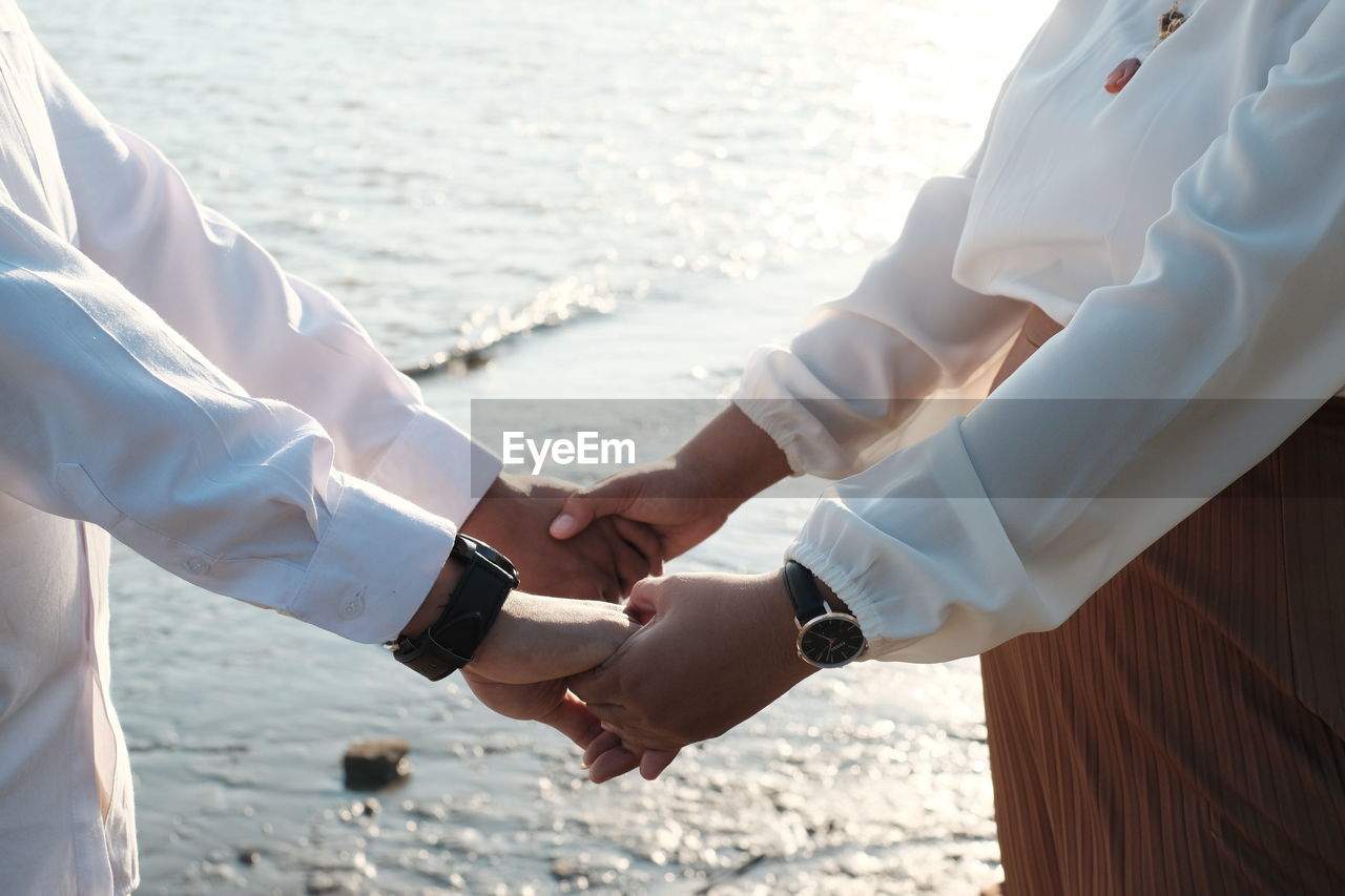 Midsection of couple holding hands at beach