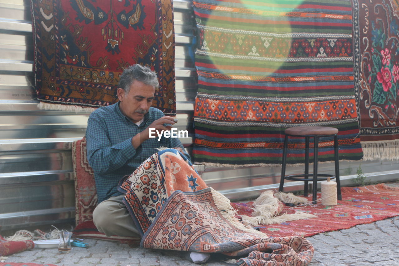 Man preparing carpet while sitting on footpath