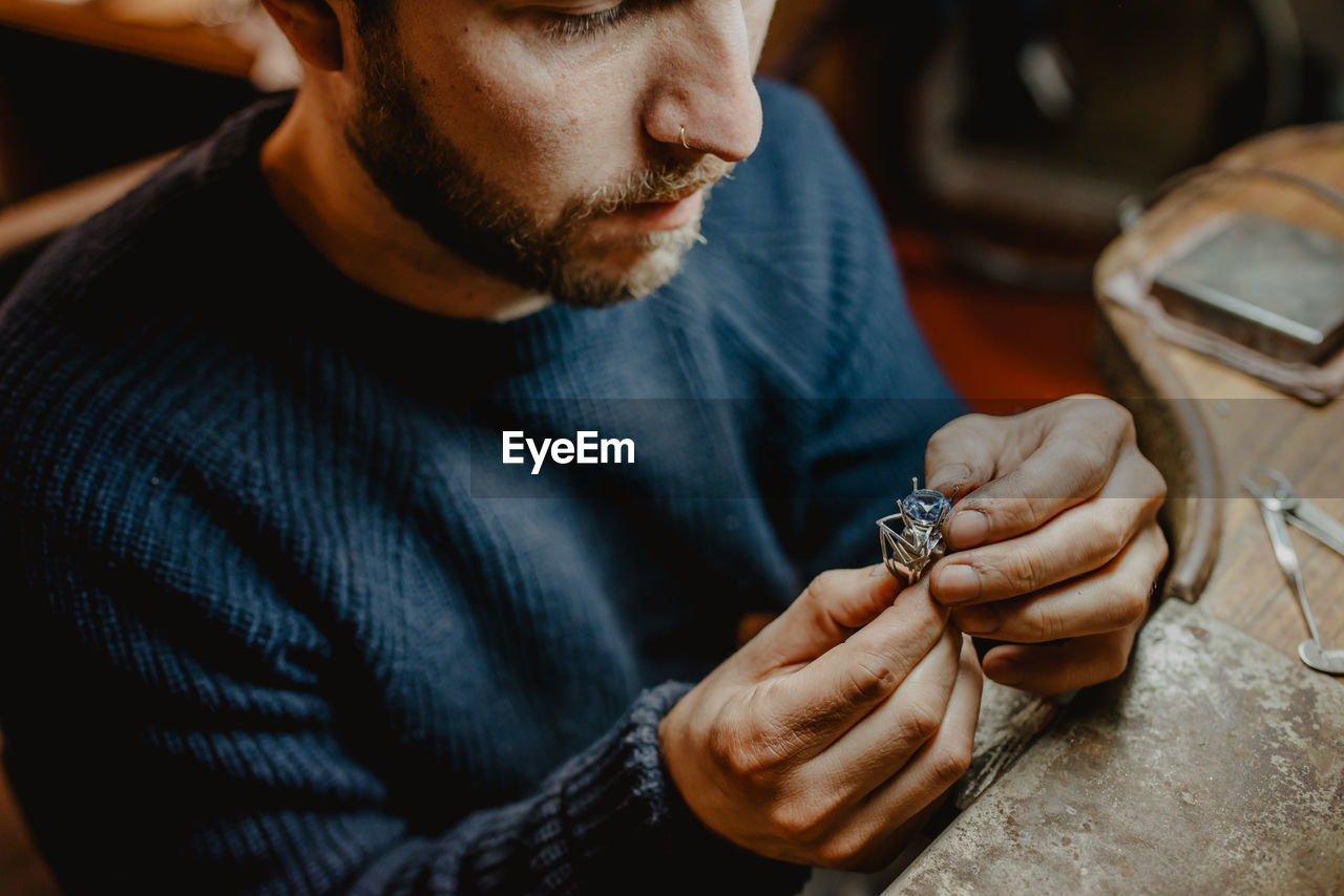 Jeweler holding unfinished ring in dirty hands and checking quality in workshop