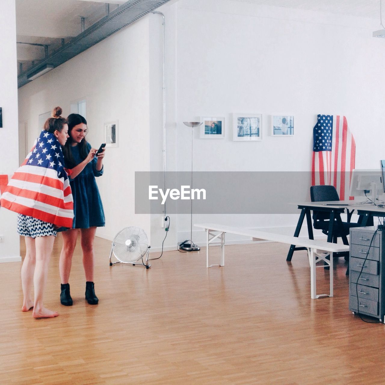 Full length of young women with american flag using mobile phone in office