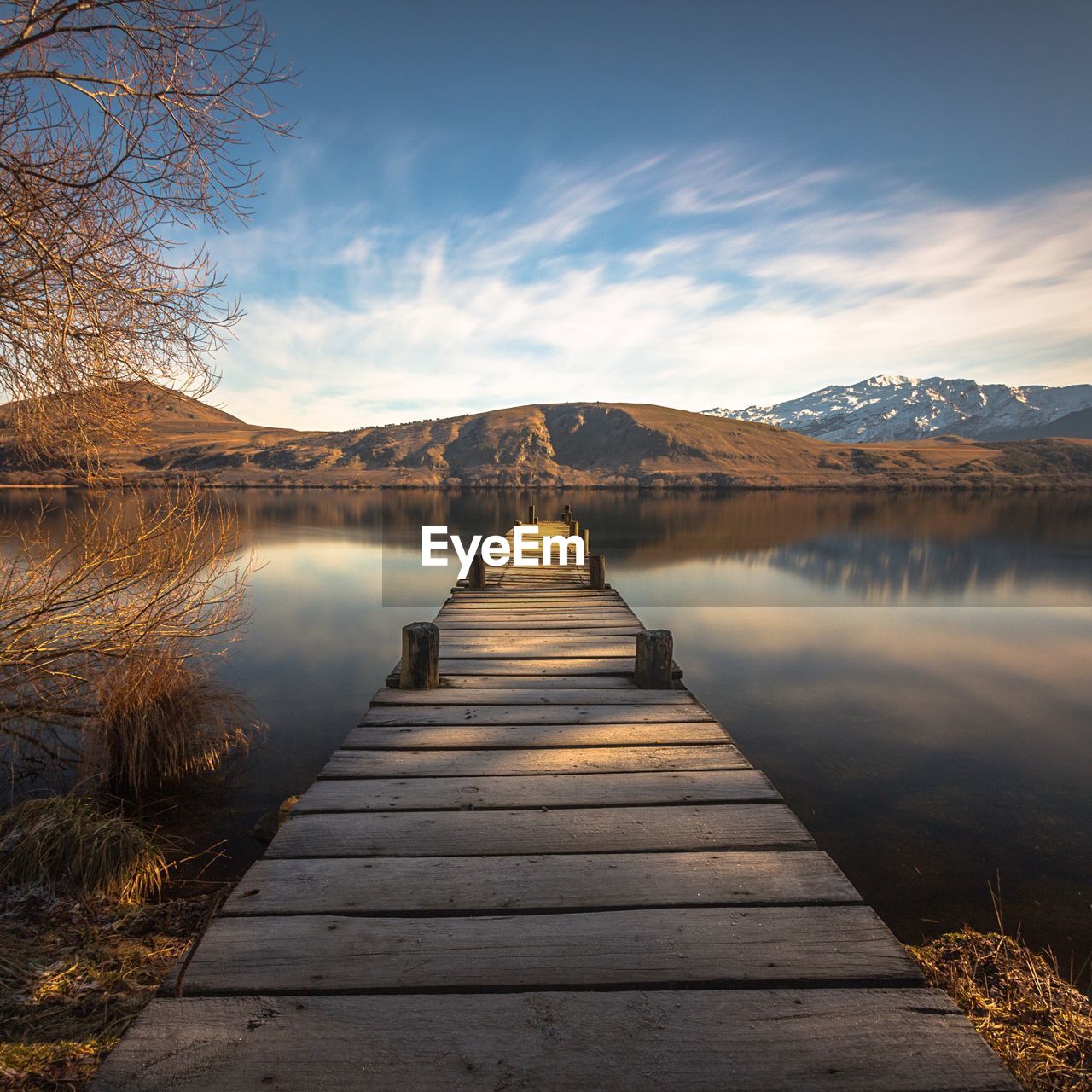 Pier over calm lake by mountains against sky