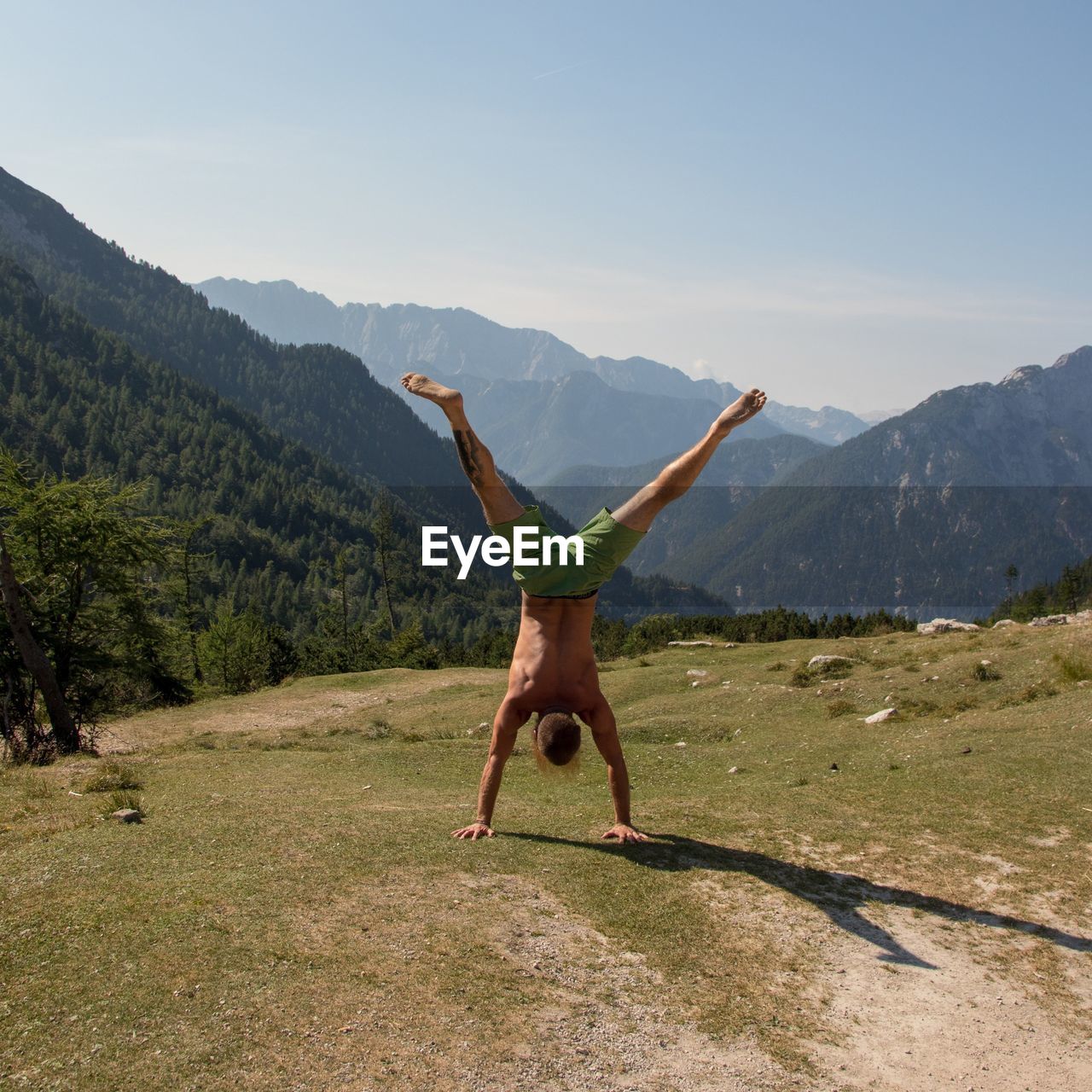 Full length rear view of shirtless man doing handstand on mountain during sunny day