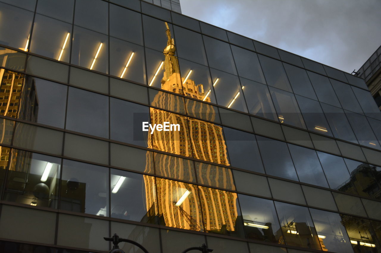 Low angle view of illuminated building reflected on windows