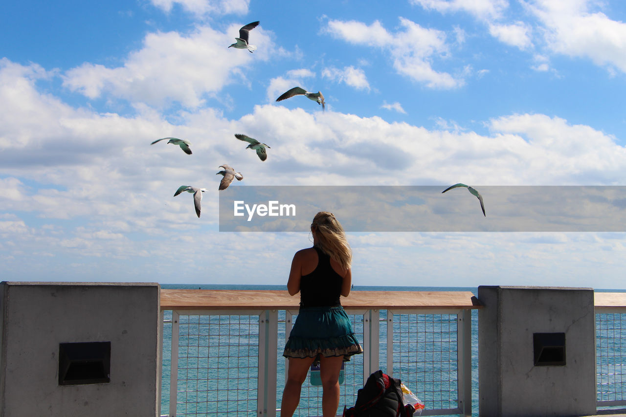 Girl looking at flying birds on miami beach against sky