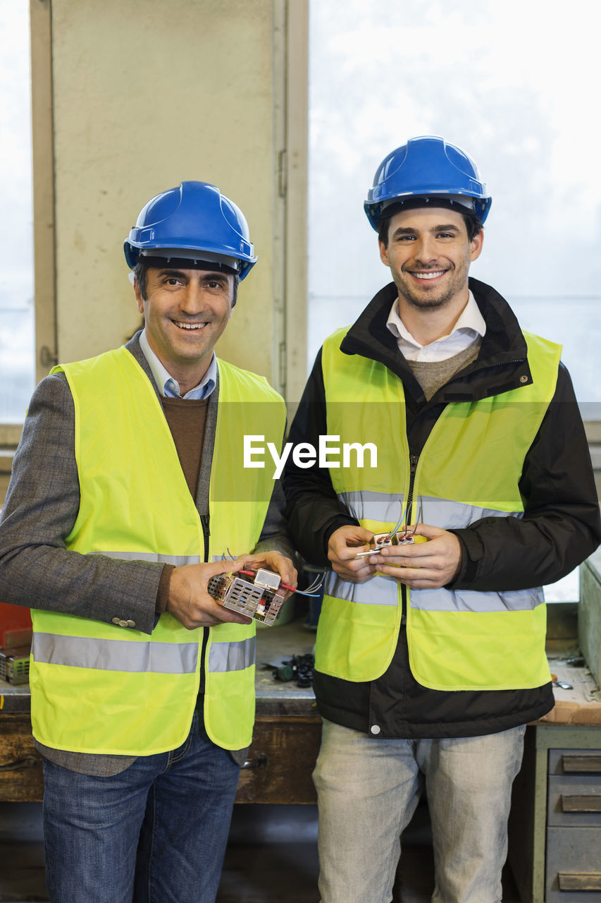 Portrait of confident manual workers holding machine part in factory