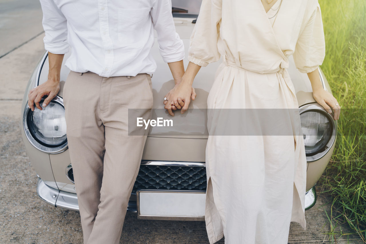 Midsection of couple holding hands while standing by car