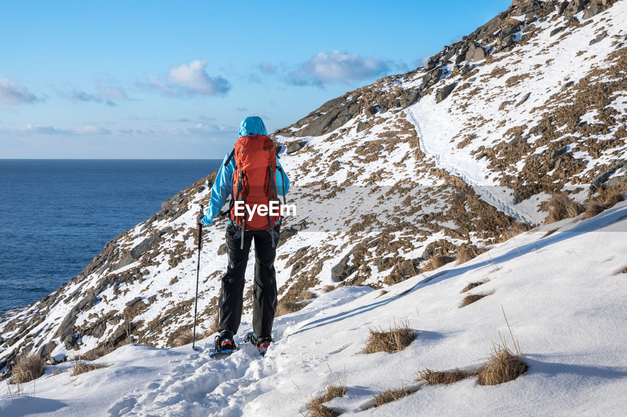 Rear view of backpack hiker standing on snow covered mountain