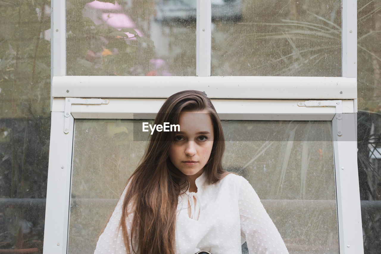 Portrait of beautiful young woman standing against window