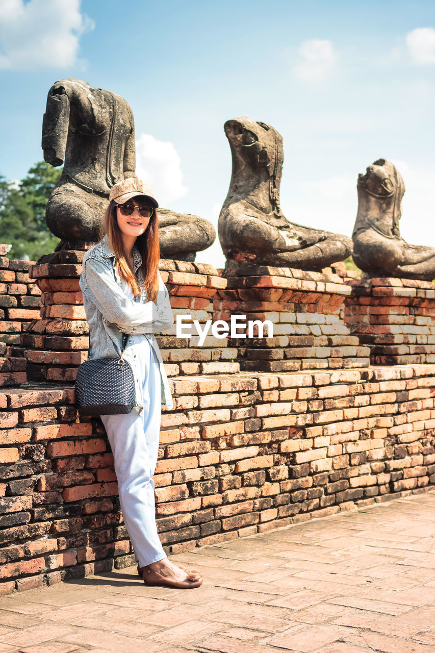 Full length of woman standing against statues on brick wall