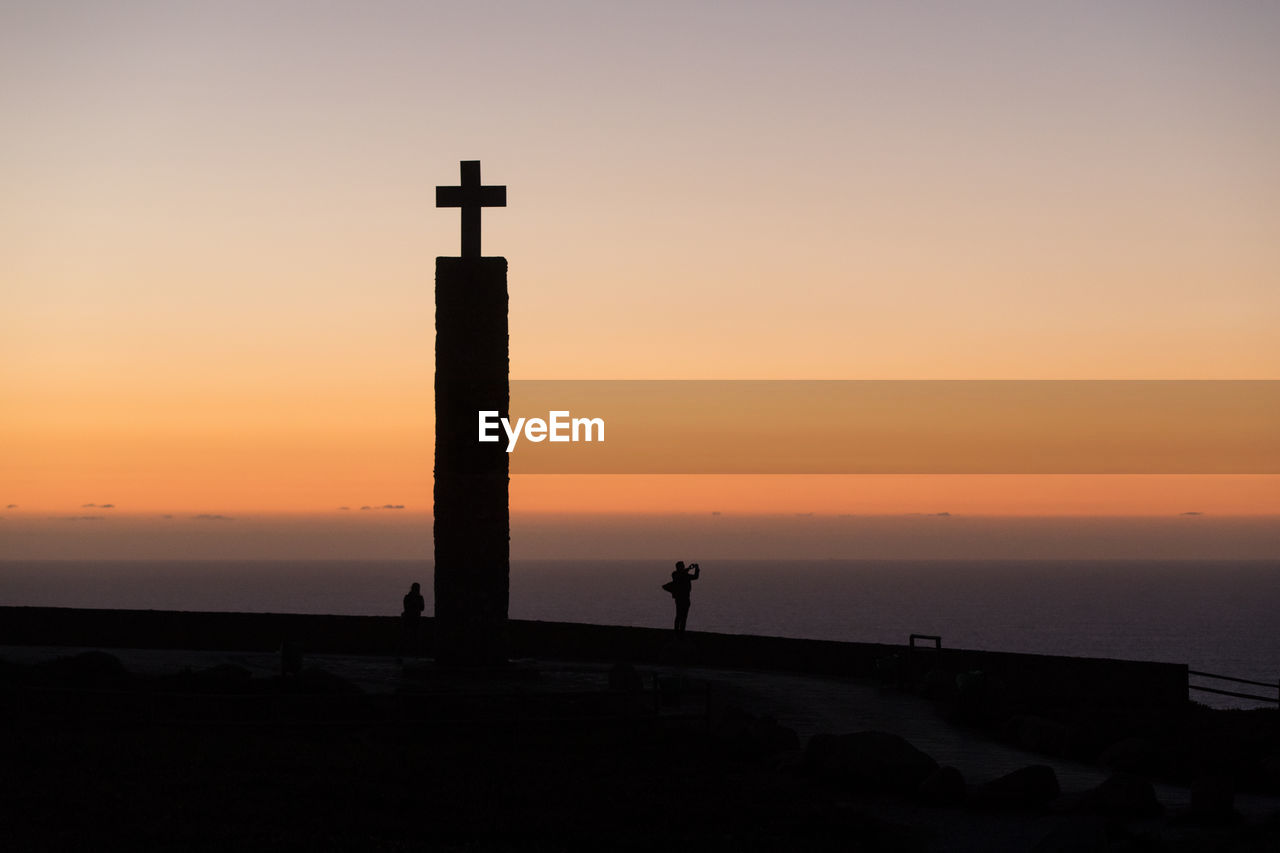 Silhouette of lighthouse at sea during sunset