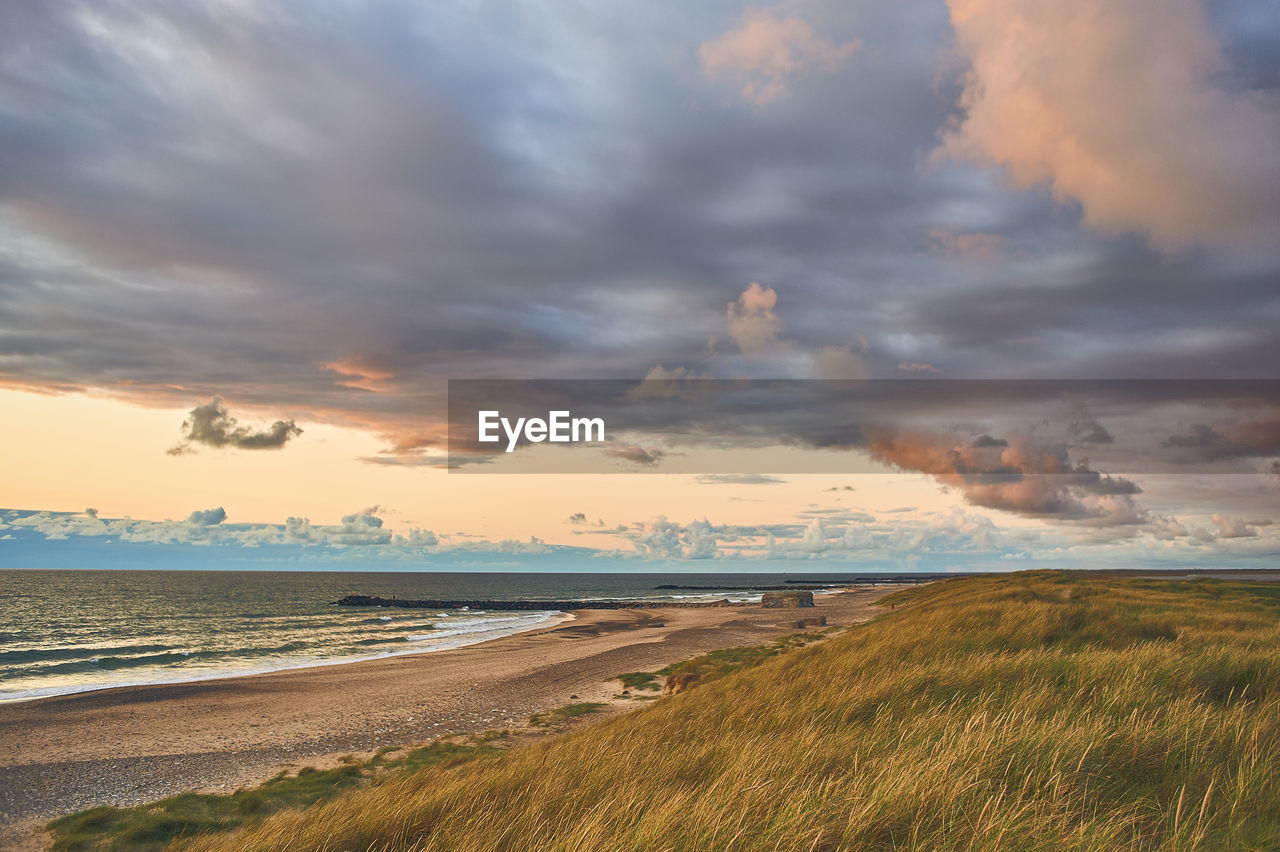 scenic view of beach against cloudy sky during sunset