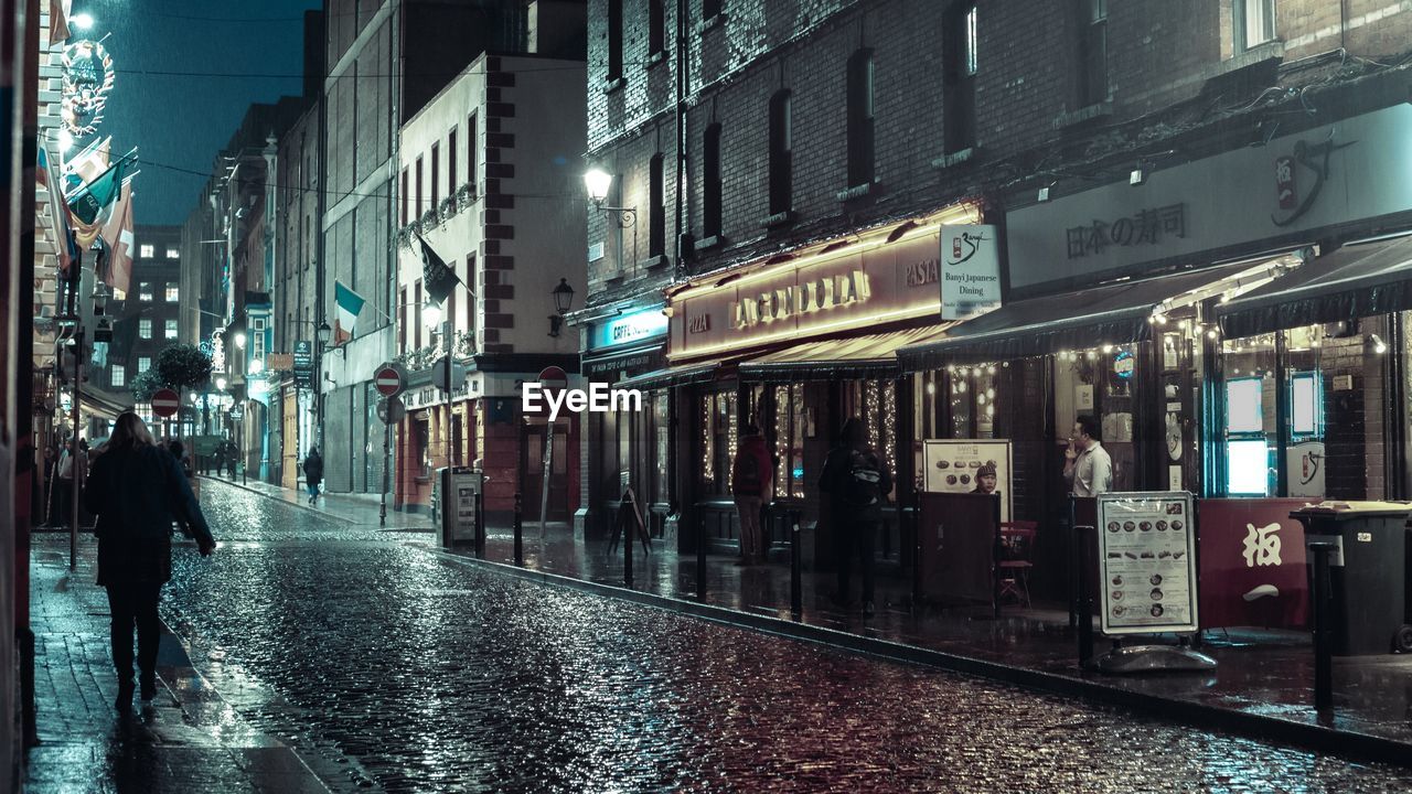 WET STREET BY ILLUMINATED BUILDINGS IN CITY