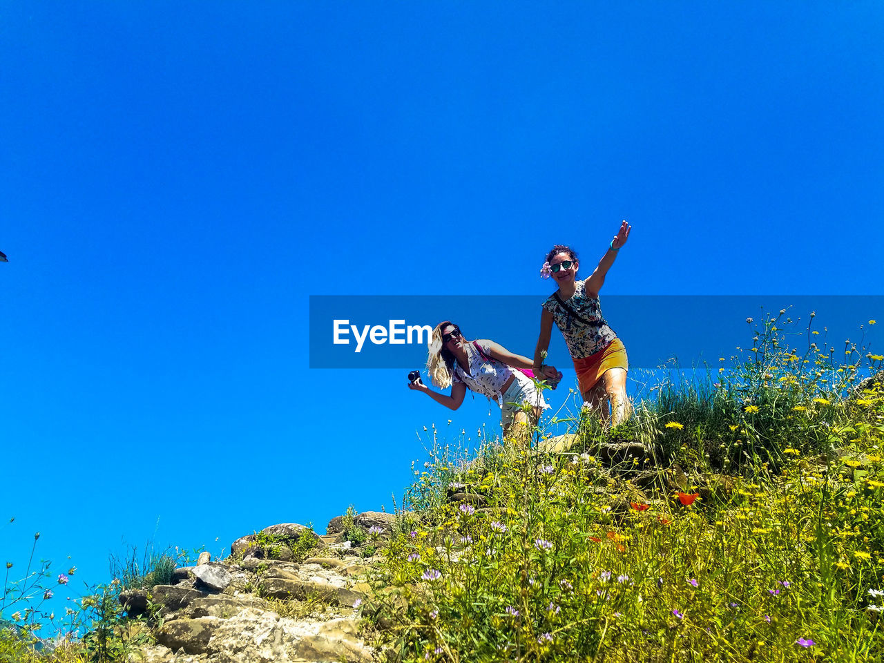 Low angle view of friends standing on mountain against clear blue sky during sunny day