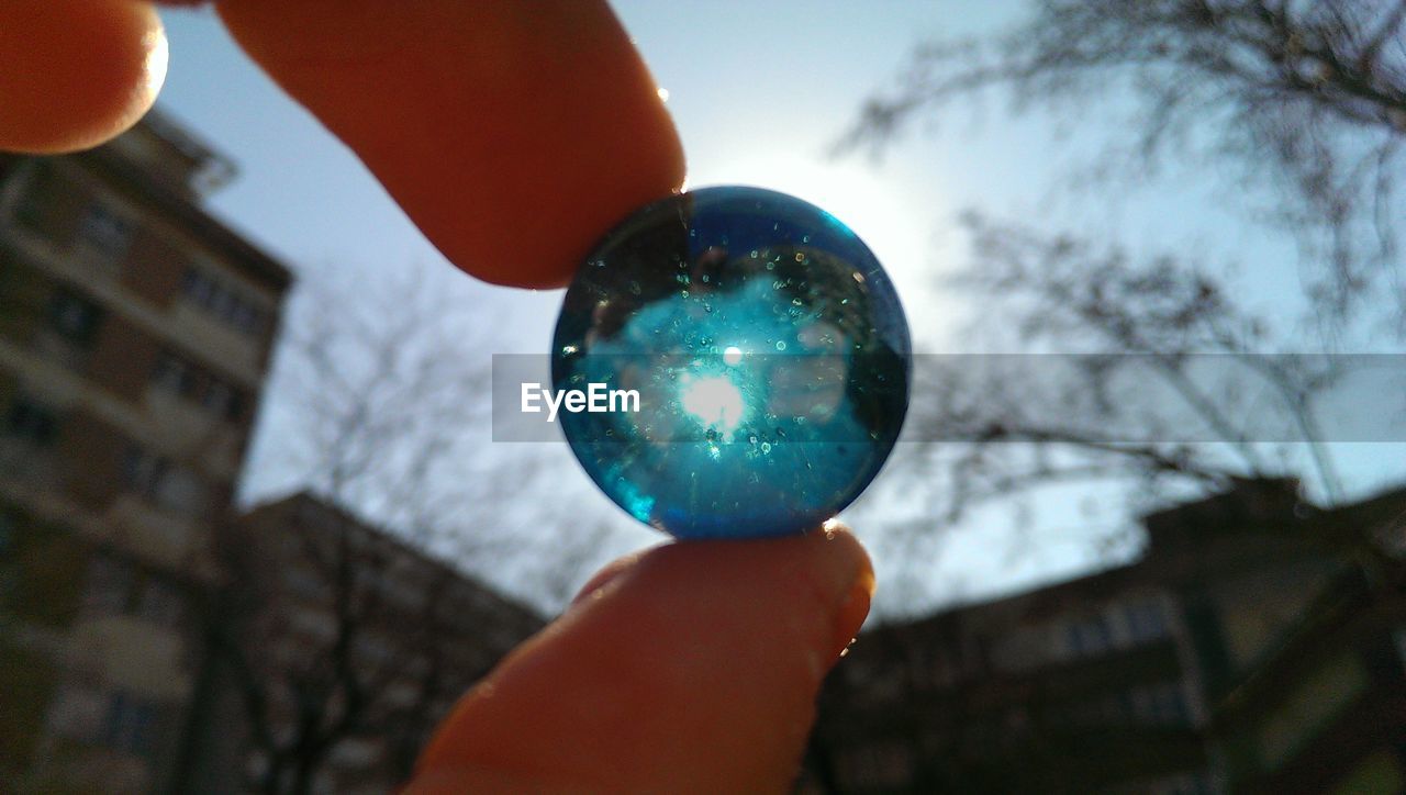 Cropped image of hand holding blue marble against sky