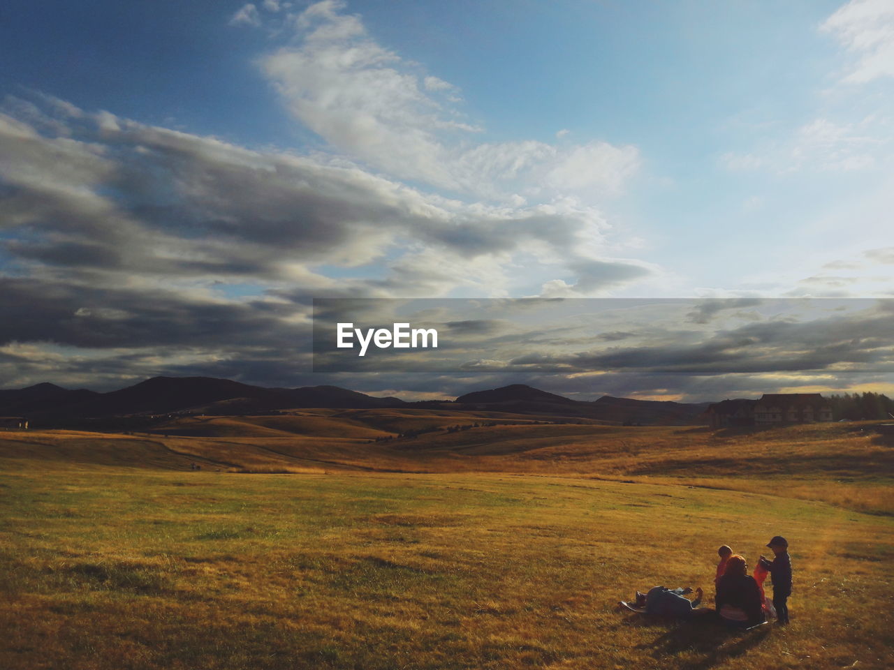 REAR VIEW OF FRIENDS SITTING ON FIELD AGAINST SKY