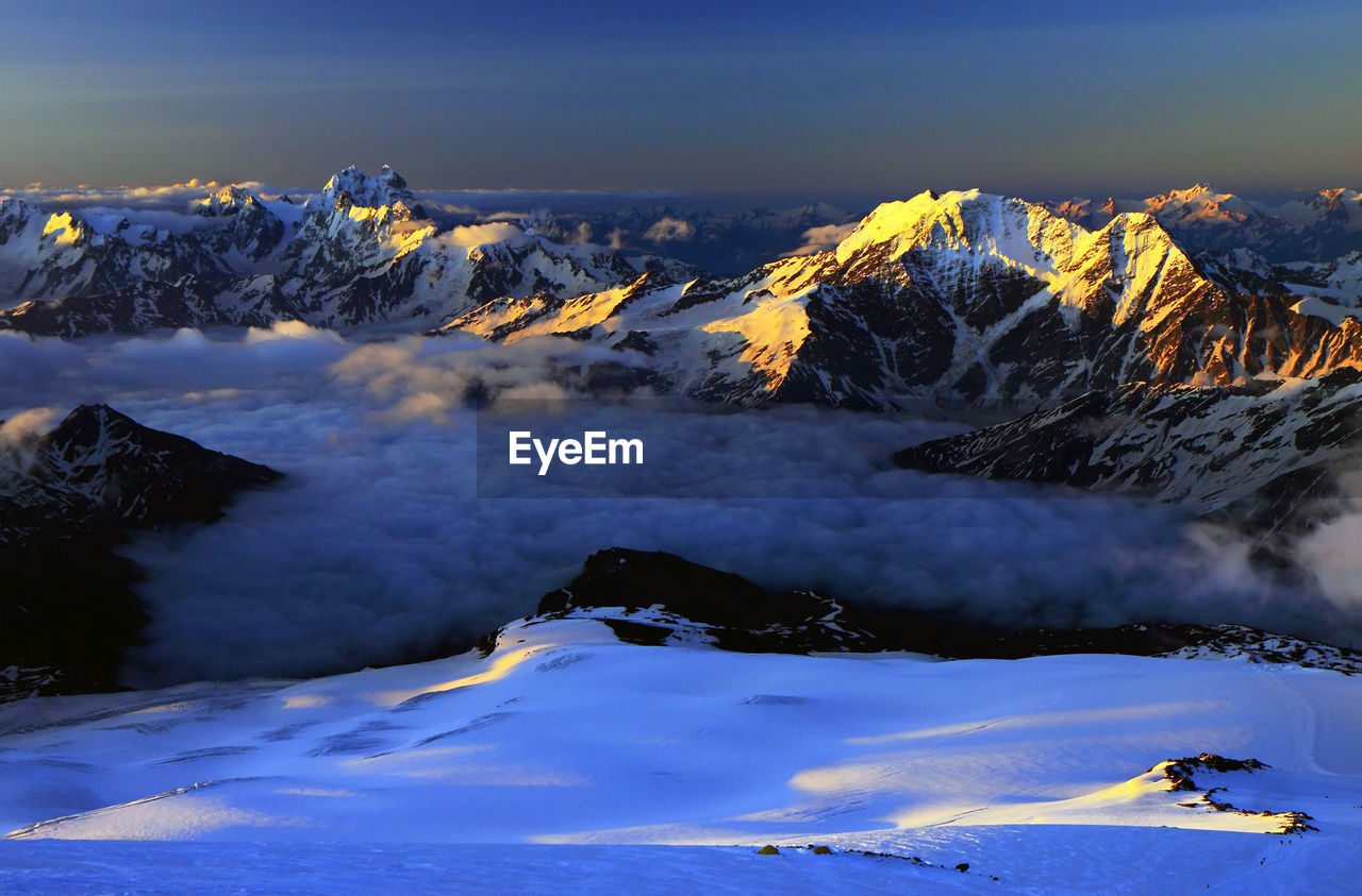 Scenic view of snowcapped mountains covered with cloudscape at sunset