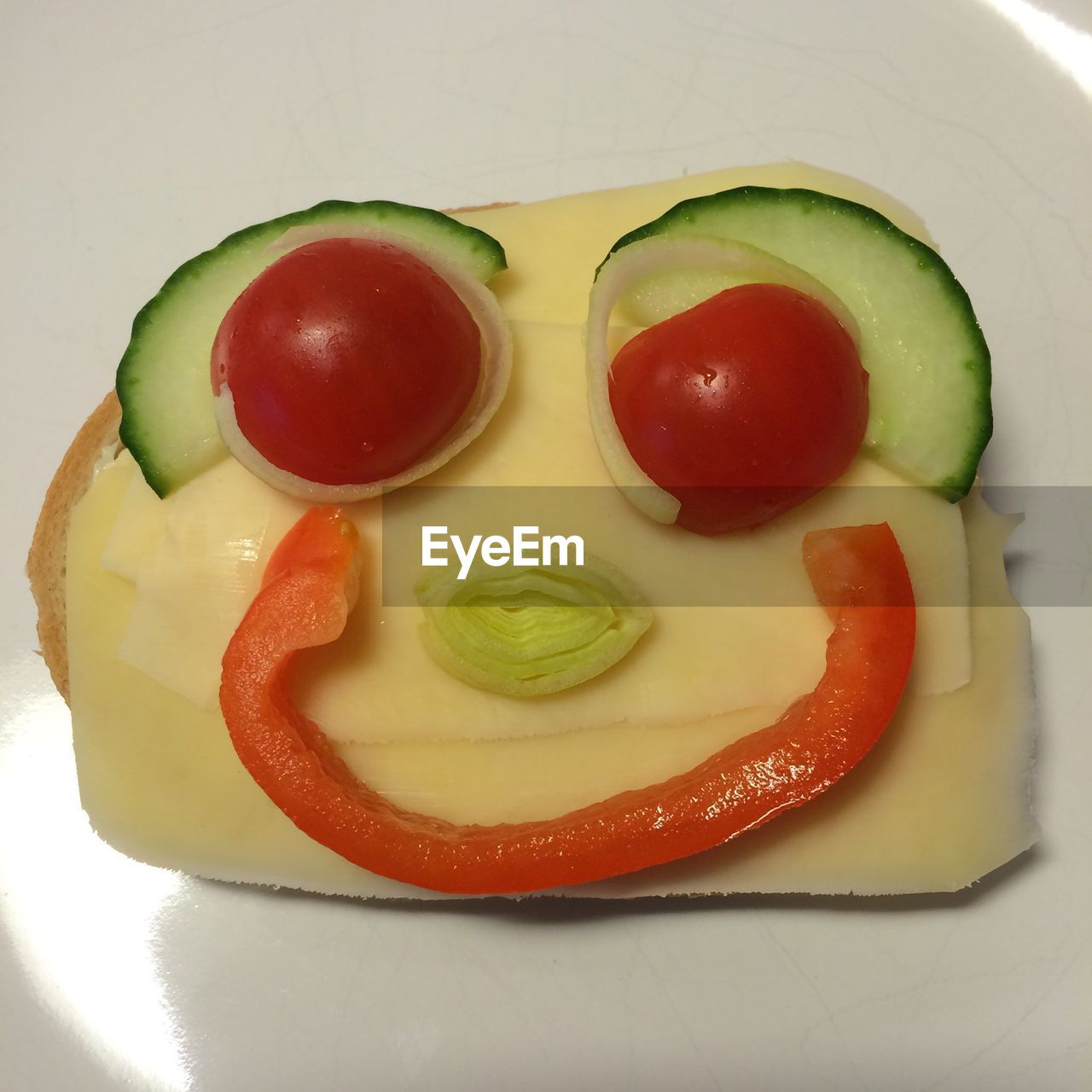 Smiley face made of vegetable and cheese on bread