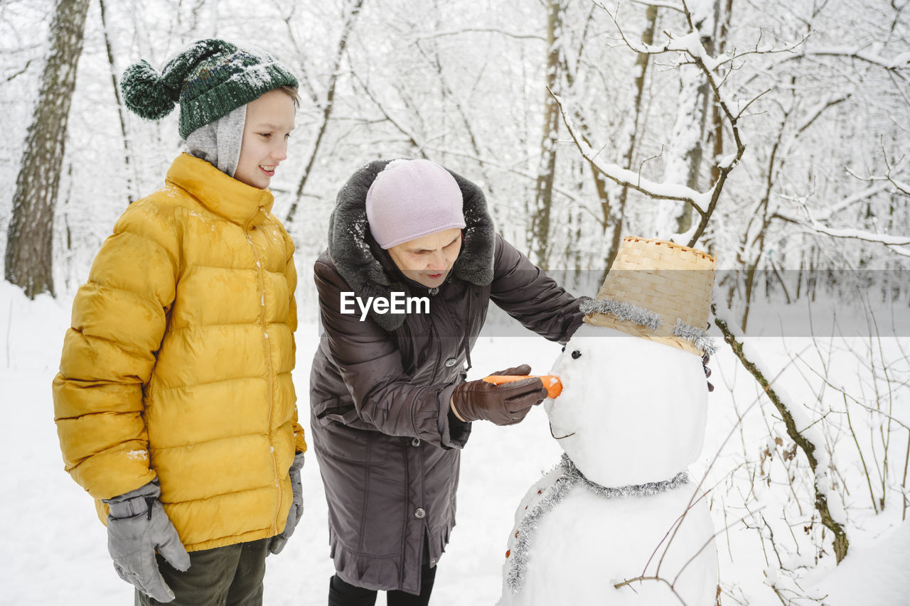 Boy making snowman with grandmother in park