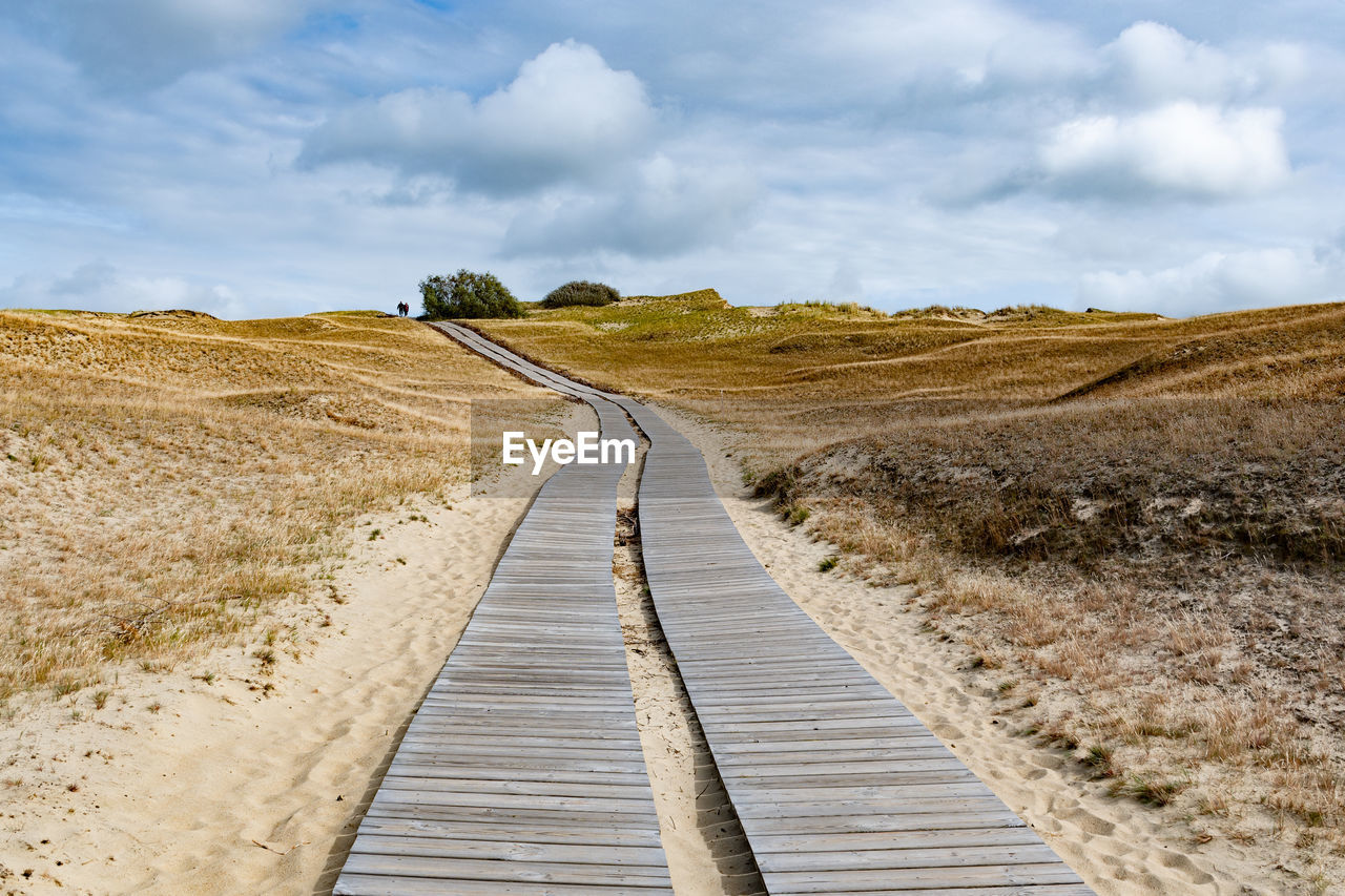 Boardwalk leading towards field against sky