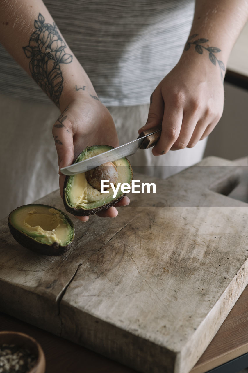 Woman cutting avocado while standing in kitchen at home