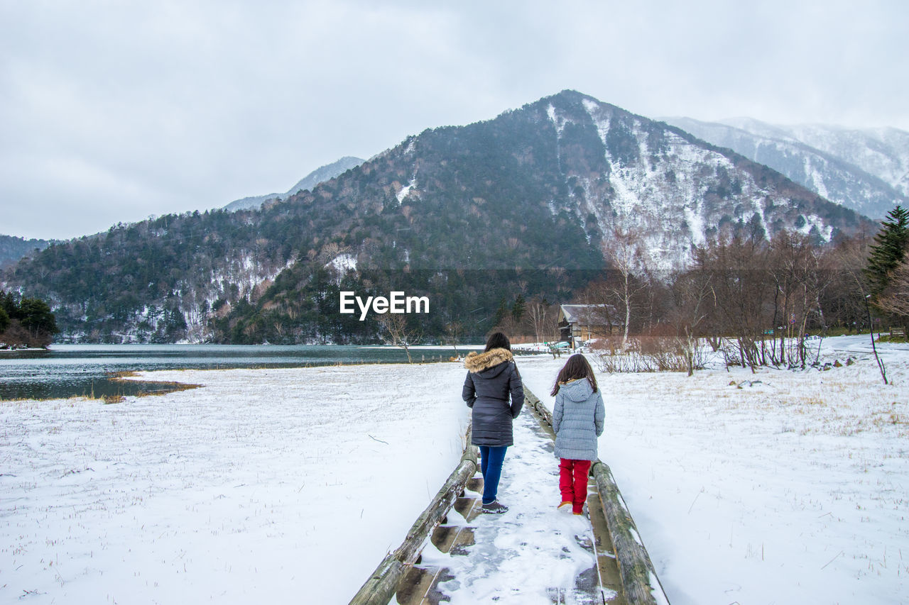 People walking on snowy pier over lake against mountains