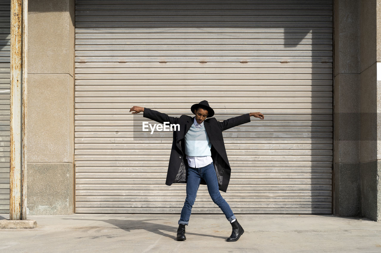 Fashionable young man dancing with arms outstretched against shutter