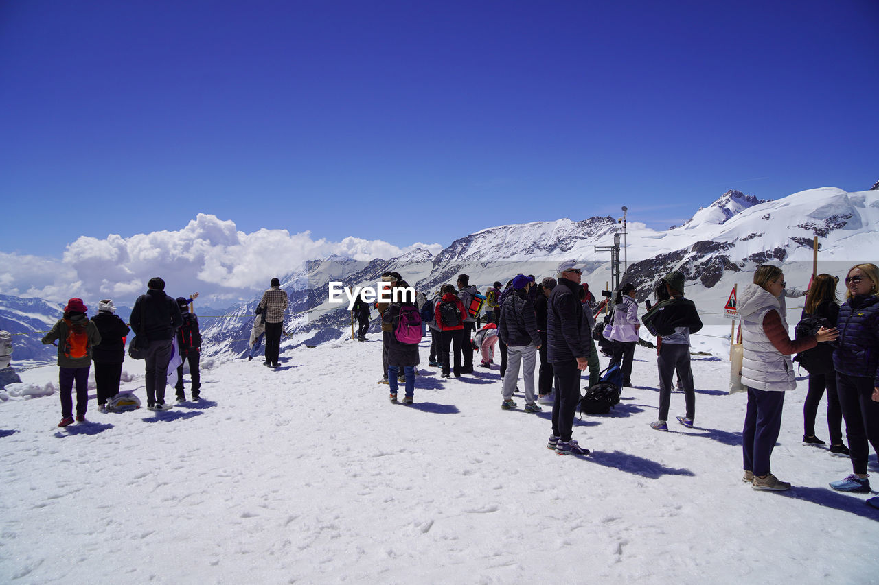 snow, winter, cold temperature, mountain, group of people, mountain range, large group of people, winter sports, sky, crowd, sports, nature, travel, leisure activity, scenics - nature, landscape, travel destinations, environment, piste, vacation, beauty in nature, ski, adventure, ski equipment, day, skiing, trip, holiday, snowcapped mountain, warm clothing, tourism, men, footwear, nordic skiing, ski mountaineering, sunlight, clear sky, adult, ice, ski holiday, clothing, frozen, blue, tourist, women, non-urban scene, outdoors, sunny, ski touring, hiking, person, lifestyles, white, walking, recreation