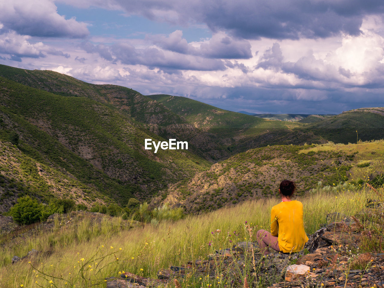 Rear view of woman sitting on mountain against cloudy sky