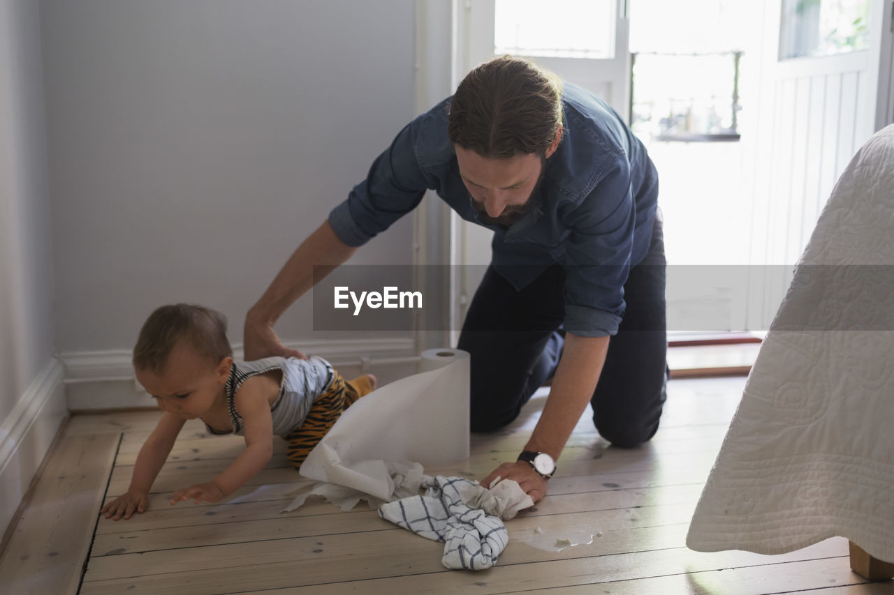 Mid adult man cleaning floor by baby boy at home