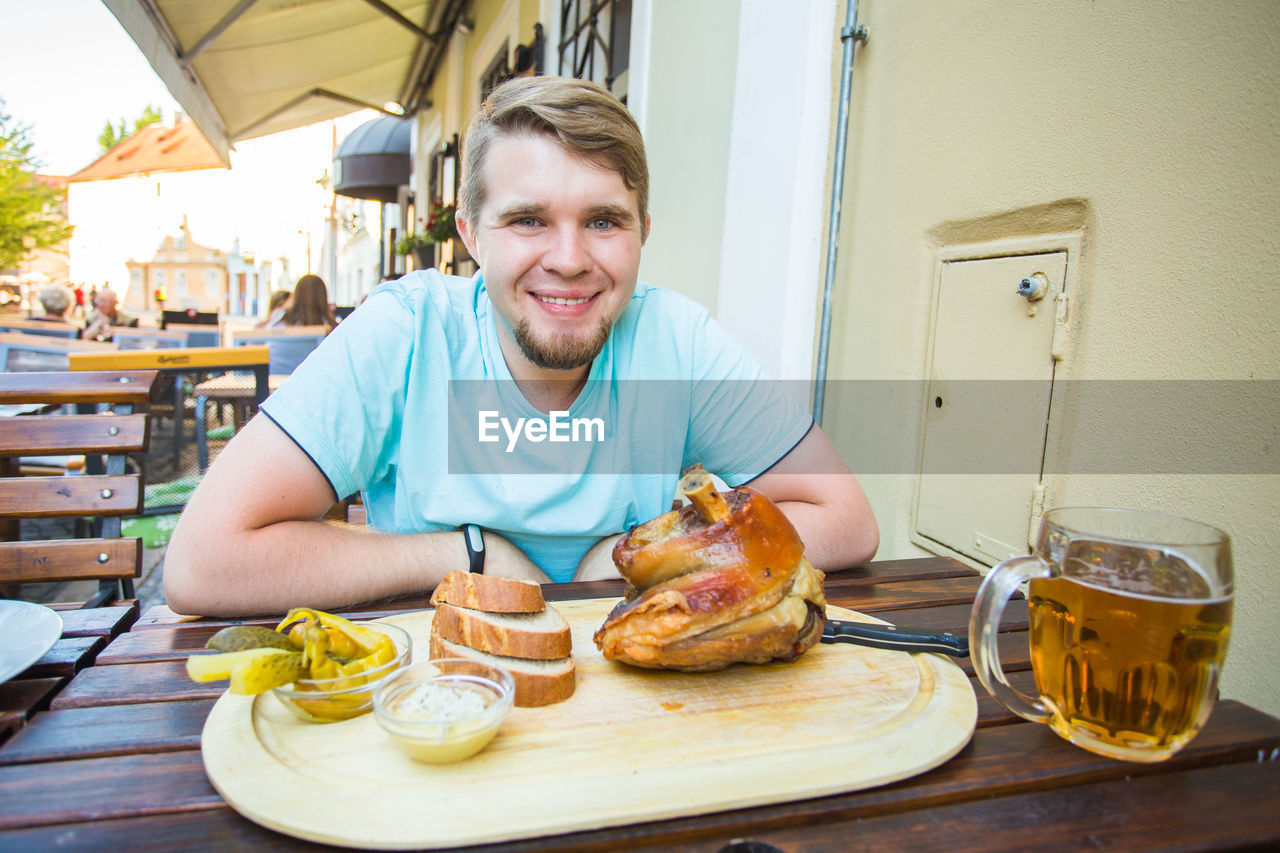 PORTRAIT OF SMILING YOUNG MAN SITTING ON TABLE