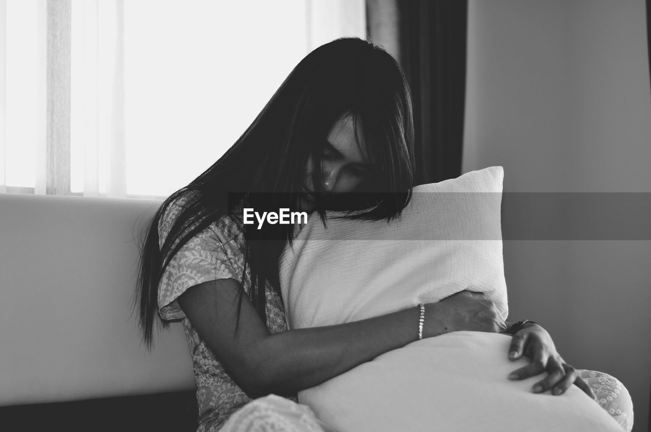 Woman embracing pillow while sitting in bedroom