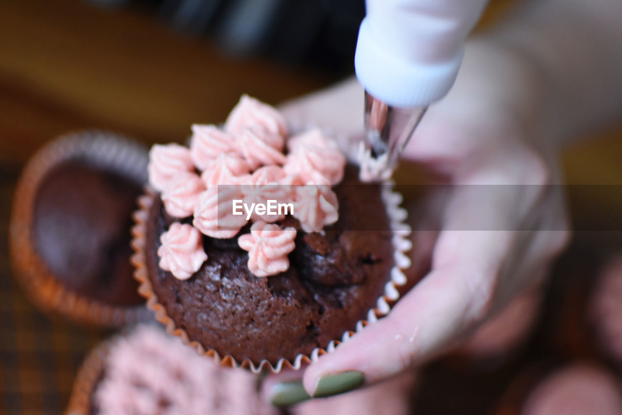 food and drink, hand, food, icing, sweetness, cake, holding, one person, adult, freshness, sweet food, dessert, chocolate, sweet, cupcake, baked, indoors, close-up, selective focus, chocolate cake, women, midsection, muffin, focus on foreground, birthday cake
