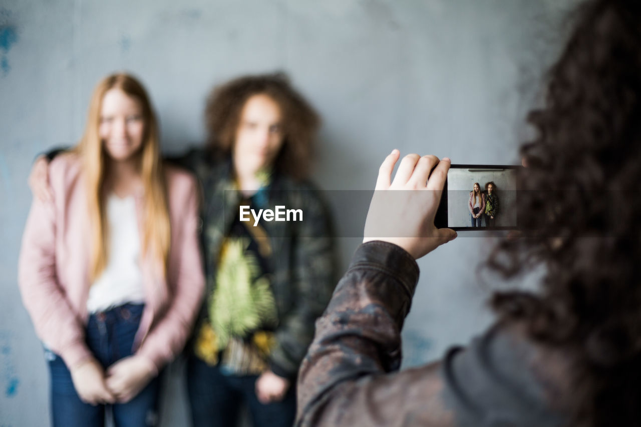 Teenage girl photographing friends standing against wall at parking garage