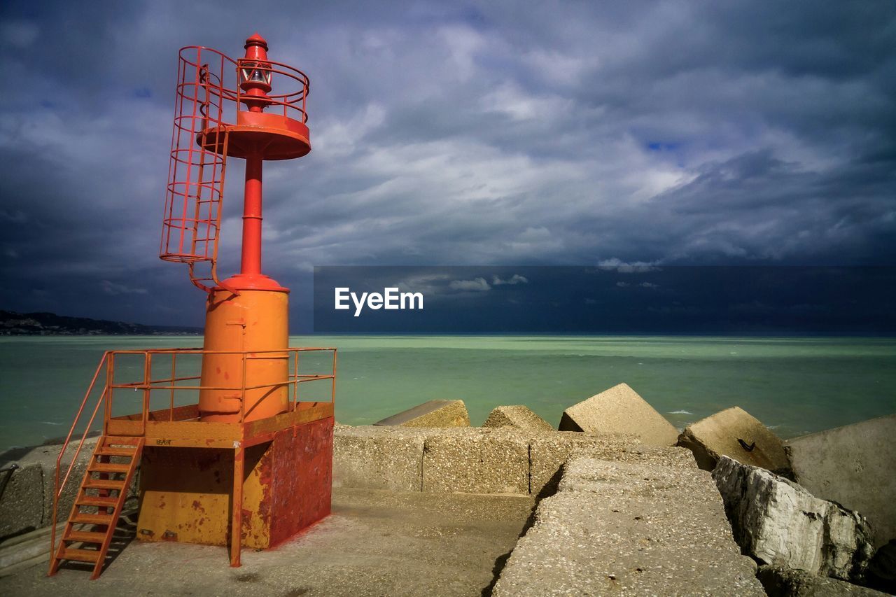 Lighthouse in sea against cloudy sky