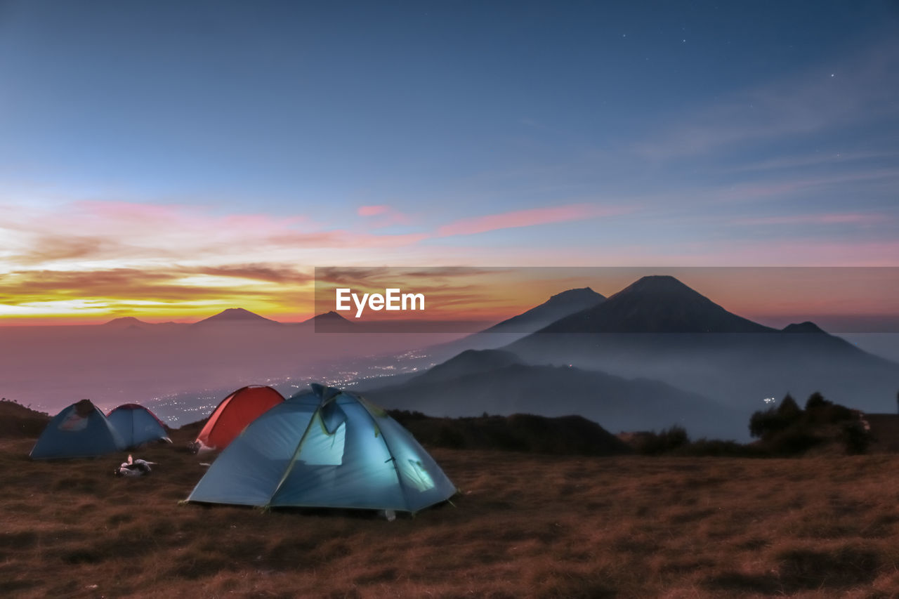 TENTS ON FIELD AGAINST SKY DURING SUNSET