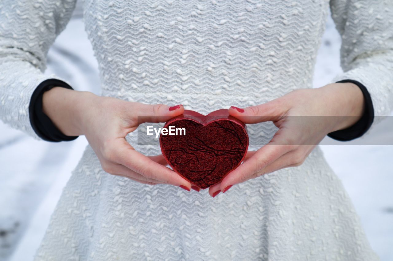 Selective focus of woman in white blouse holding a red heart-shaped box in her hands