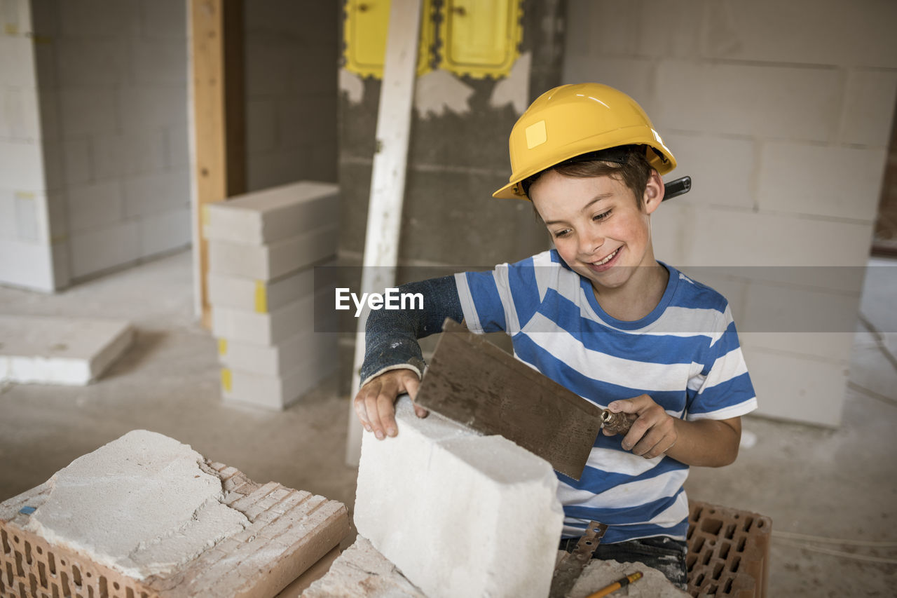 Boy with hardhat cutting block while standing at attic during renovation