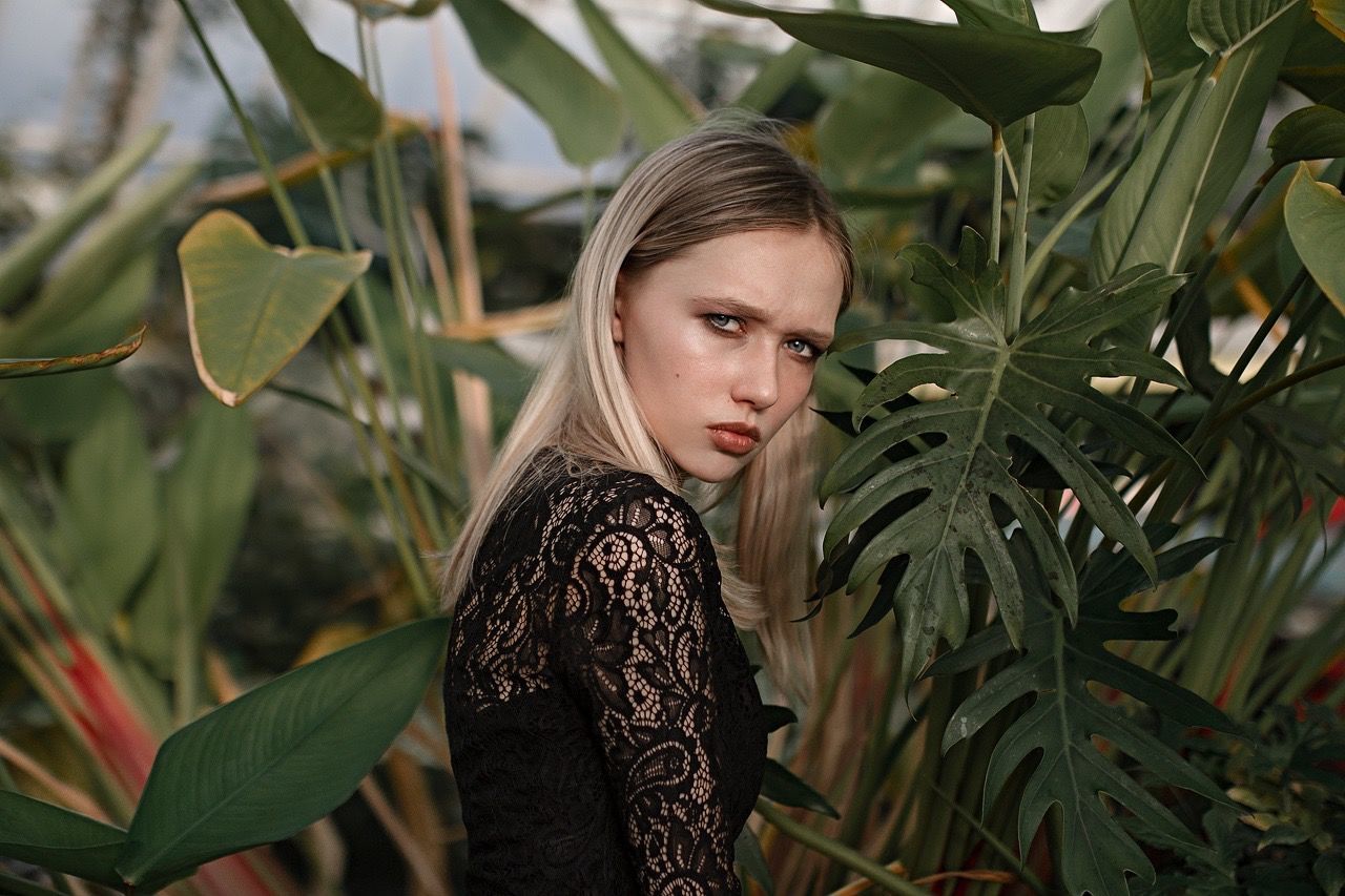 CLOSE-UP PORTRAIT OF YOUNG WOMAN WITH PLANTS IN FOREGROUND