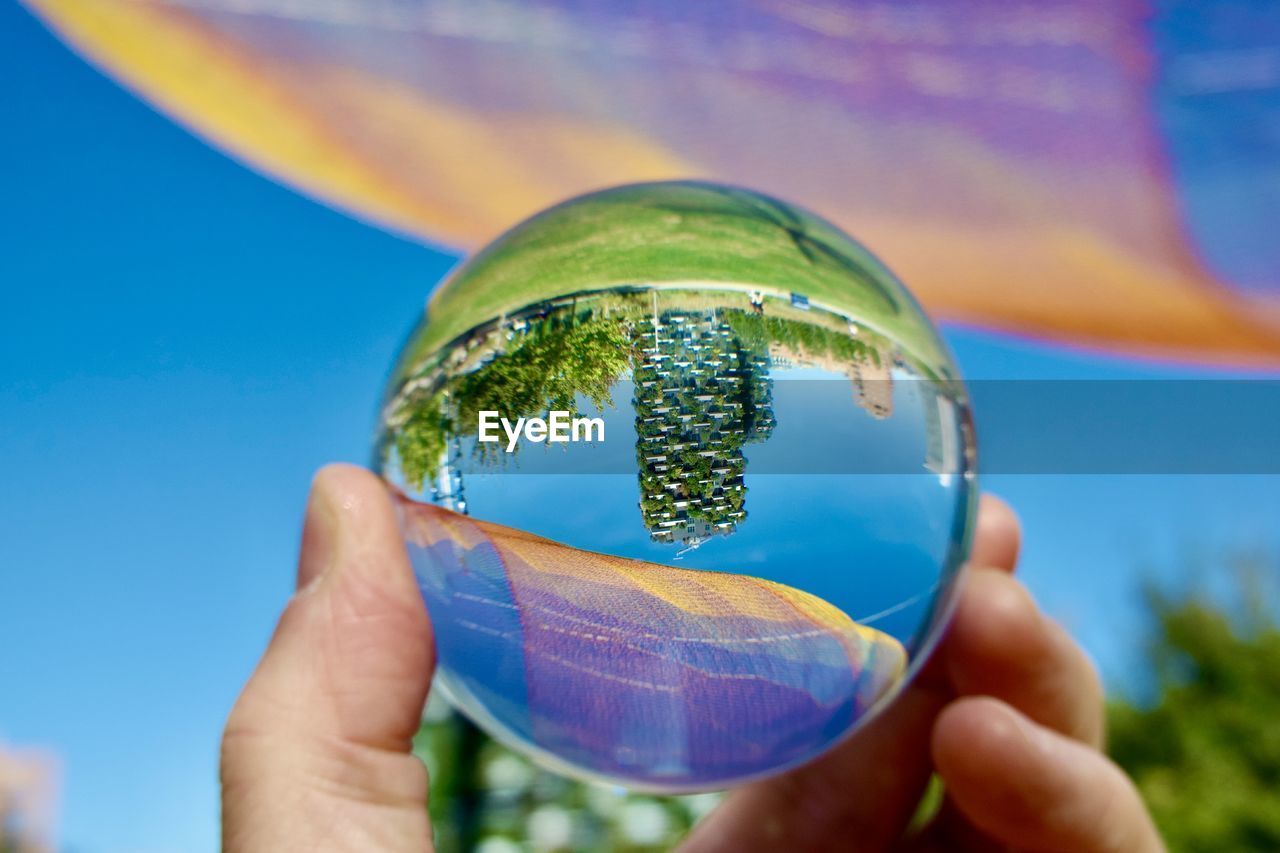 holding, blue, hand, sphere, nature, one person, sky, close-up, transparent, globe - man made object, green, focus on foreground, yellow, outdoors, glass, day, environment, planet earth, liquid bubble, bubble, reflection, crystal ball, plant, environmental conservation, adult, sunlight, space, fragility