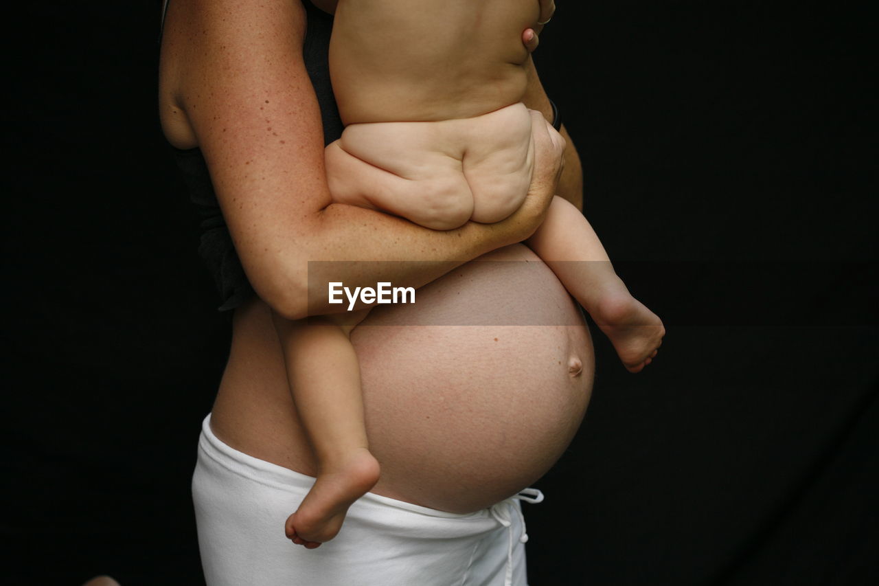 Midsection of pregnant mother with naked baby against black background