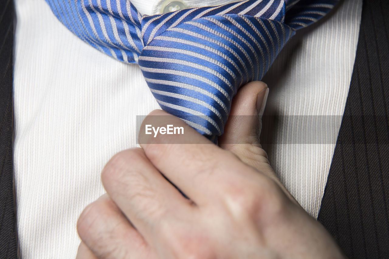 Midsection of businessman adjusting necktie