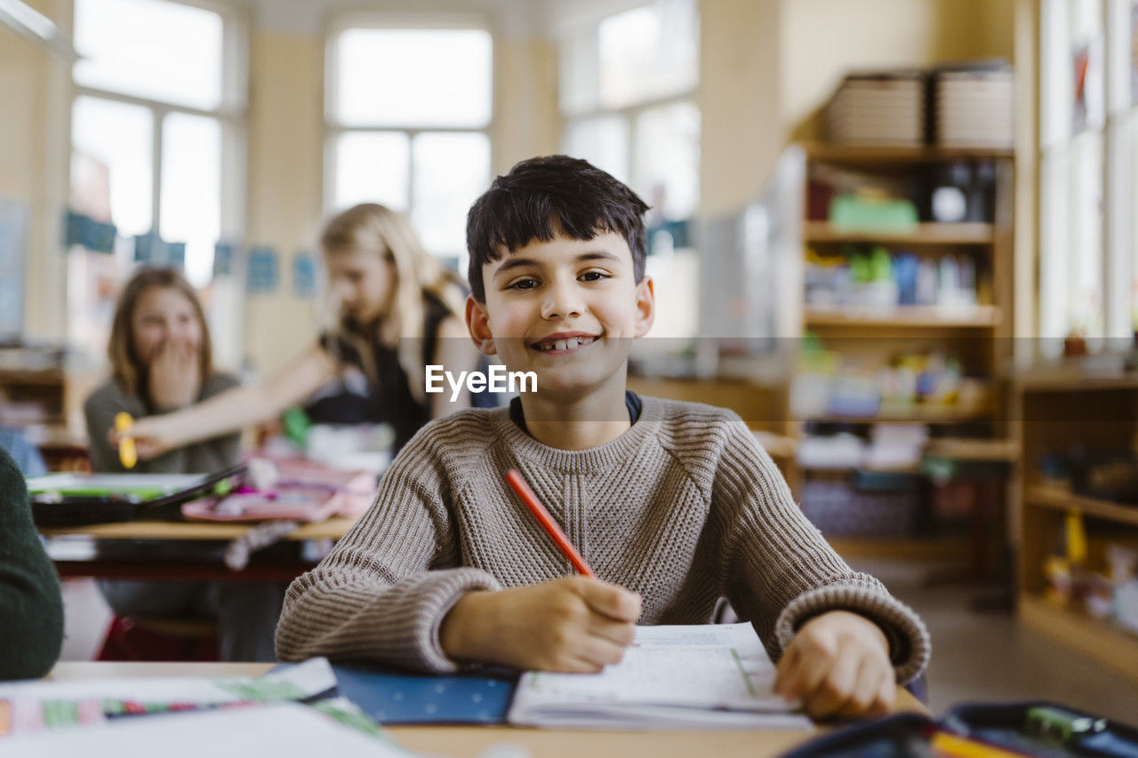 Portrait of happy male pupil sitting at desk in classroom