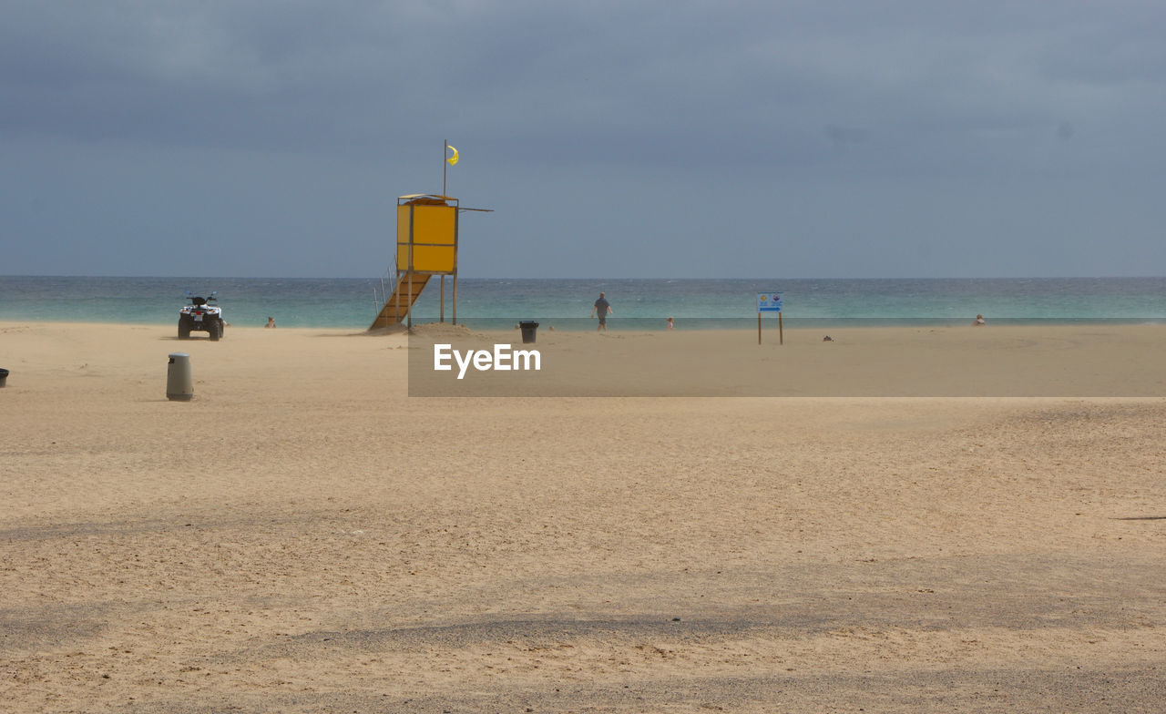 MAN STANDING ON BEACH BY SEA AGAINST SKY