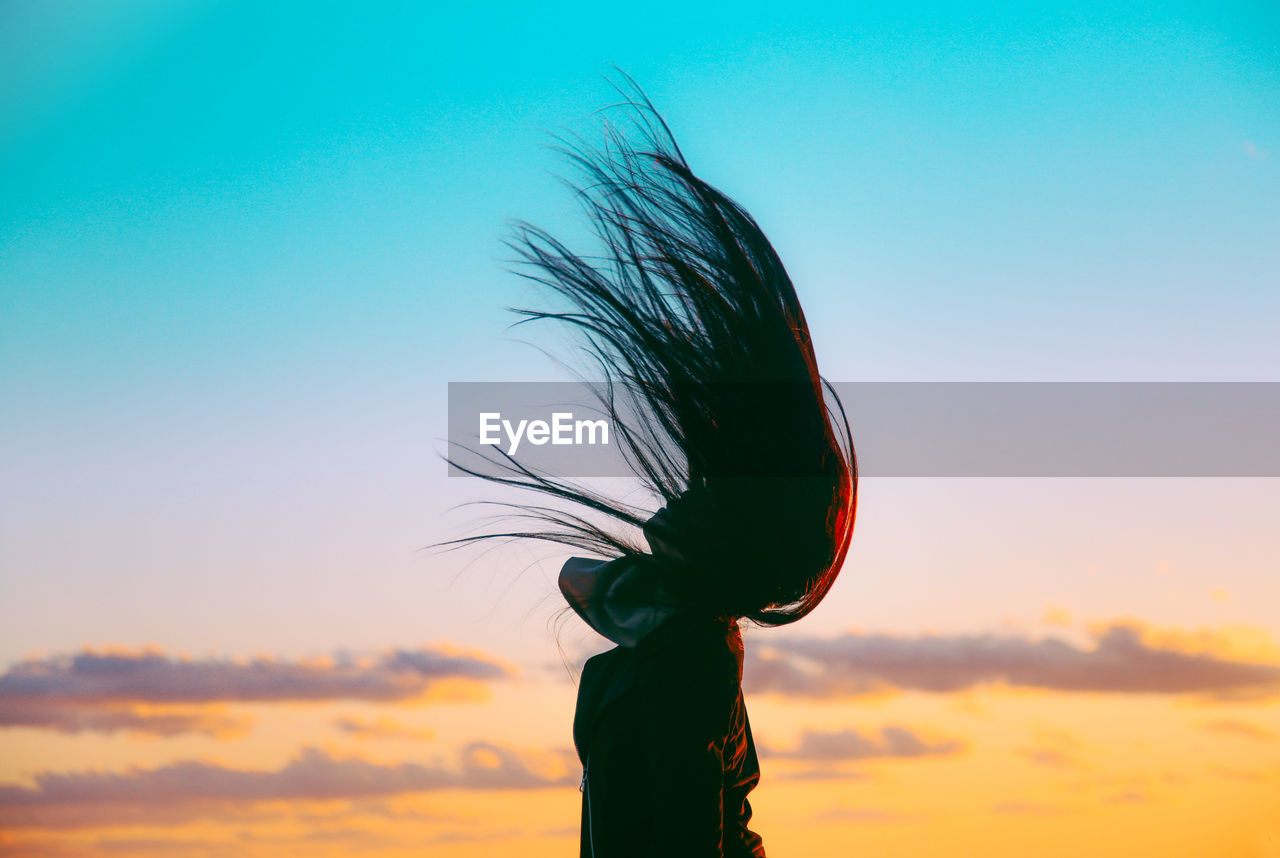 Woman tossing hair against sky during sunset