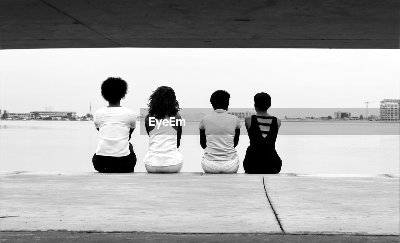 Rear view of friends sitting on jetty against sea