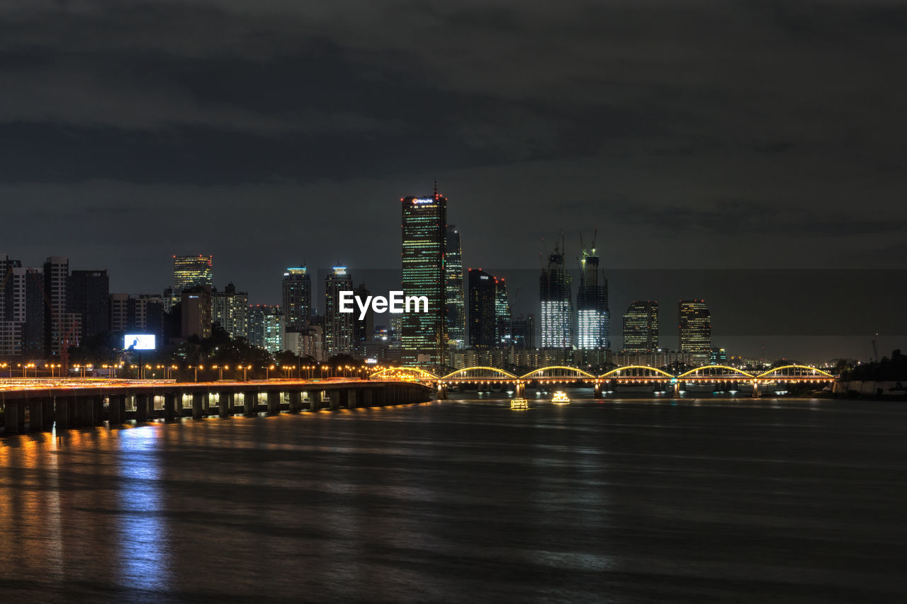 Illuminated city by river against sky at night