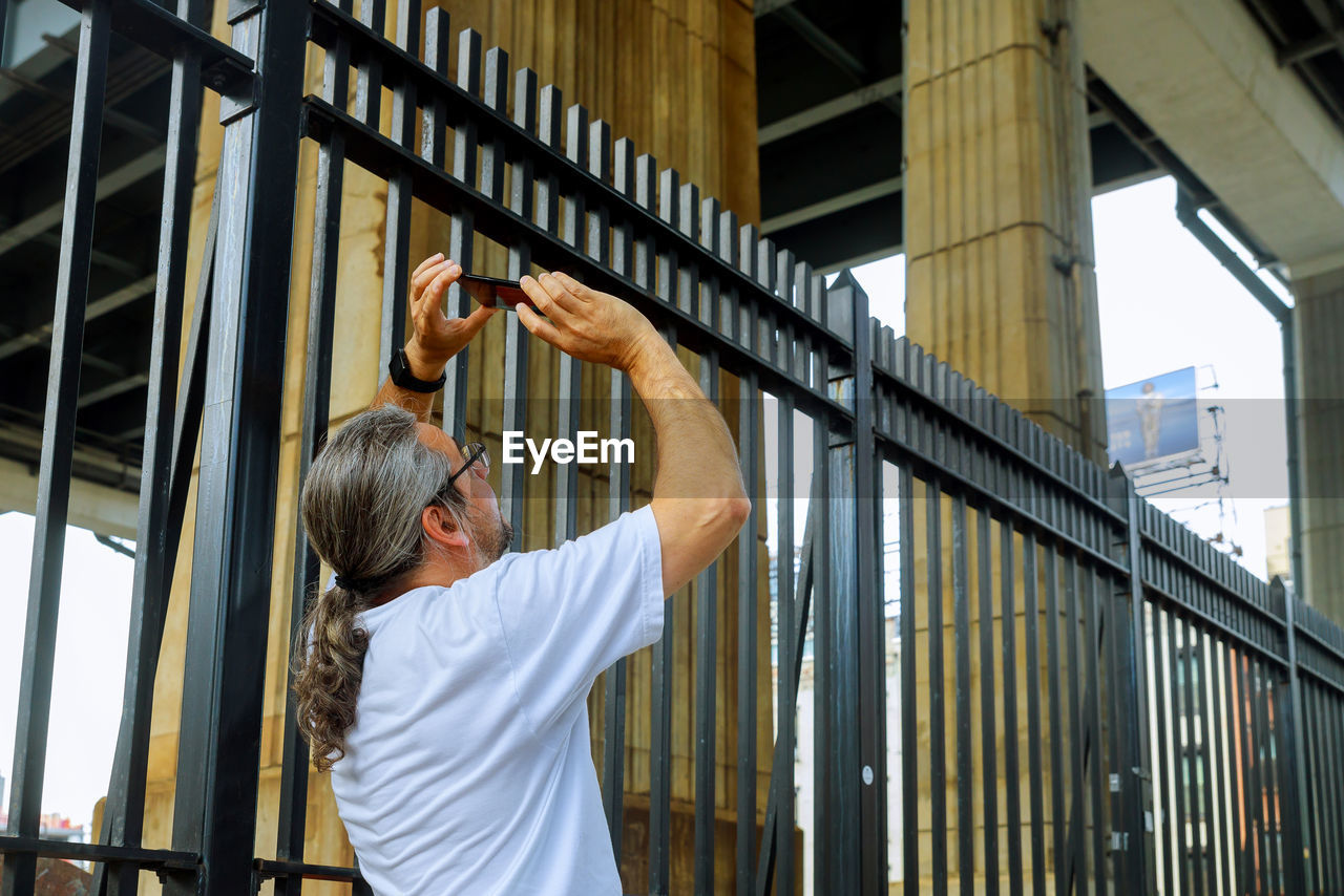 Mature man photographing while standing by fence