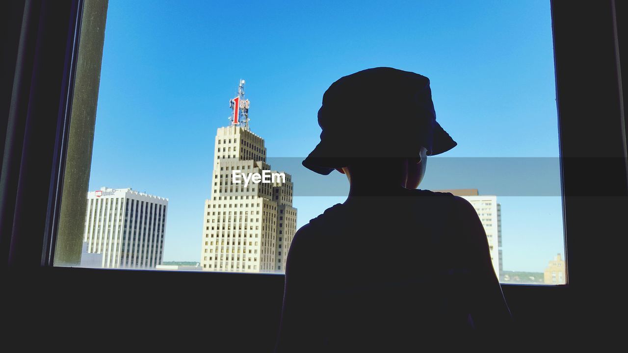 Rear view of silhouette boy looking through window